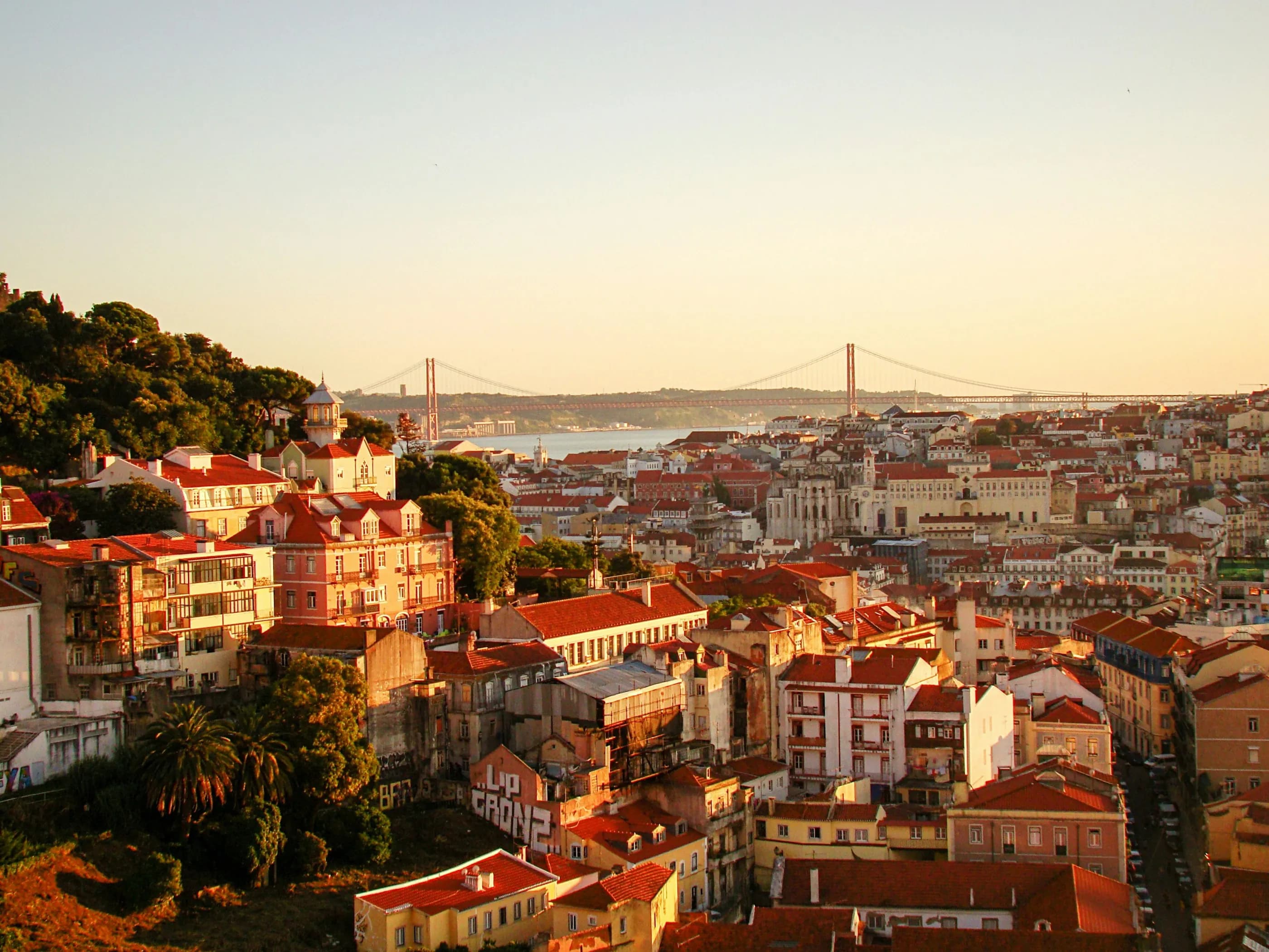 Lisbon rooftops at golden hour, with the 25 de Abril Bridge in the distance